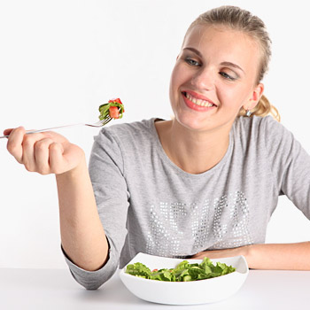 immagine di una ragazza sorridente che mangia un piatto di verdura