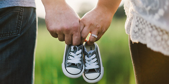 Immagine delle mani di una coppia che tengono insieme delle scarpe da bambino