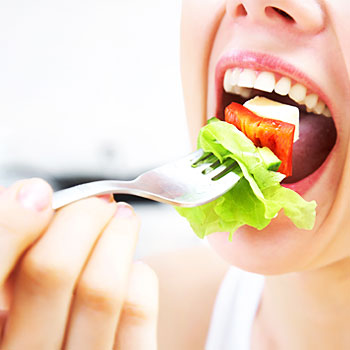 particolare di una bocca di donna che mangia insalata